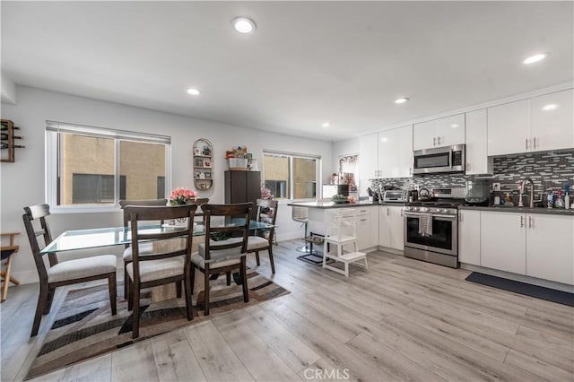 kitchen featuring white cabinetry, light hardwood / wood-style flooring, appliances with stainless steel finishes, kitchen peninsula, and backsplash