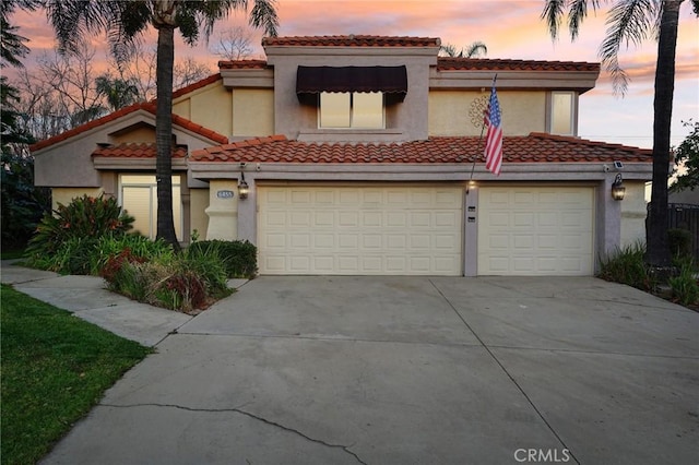 mediterranean / spanish home featuring a garage, a tiled roof, concrete driveway, and stucco siding