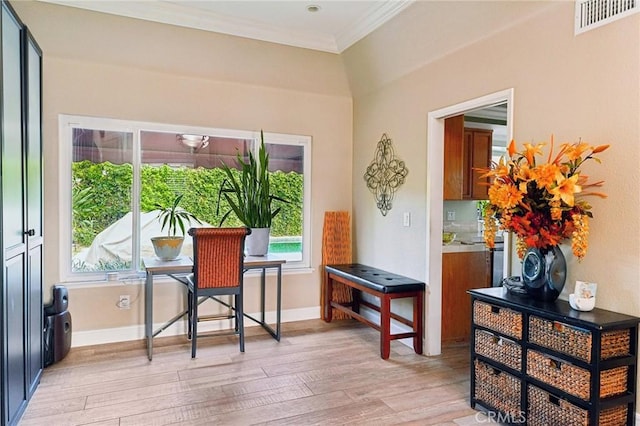 interior space featuring baseboards, light wood-type flooring, visible vents, and crown molding