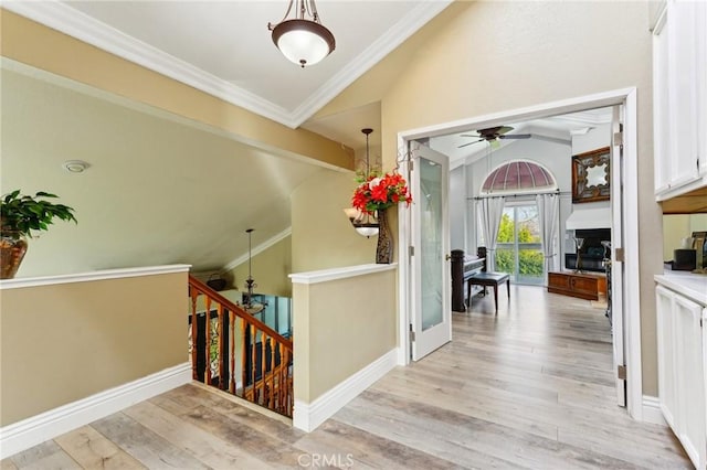 corridor with light wood-style flooring, lofted ceiling with beams, ornamental molding, an upstairs landing, and baseboards