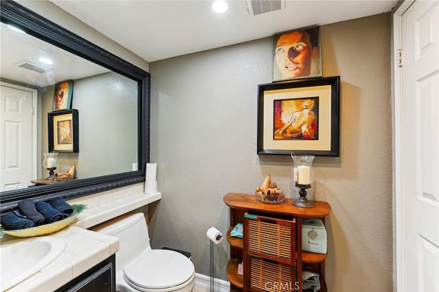 half bathroom with toilet, visible vents, vanity, and recessed lighting