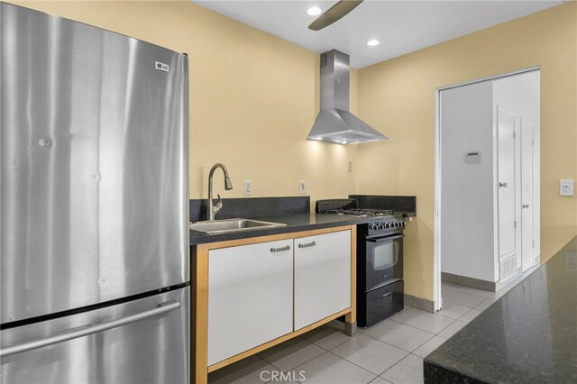 kitchen with light tile patterned floors, freestanding refrigerator, a sink, black gas stove, and wall chimney exhaust hood