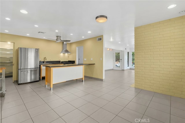 kitchen with dark countertops, freestanding refrigerator, a sink, brick wall, and wall chimney exhaust hood