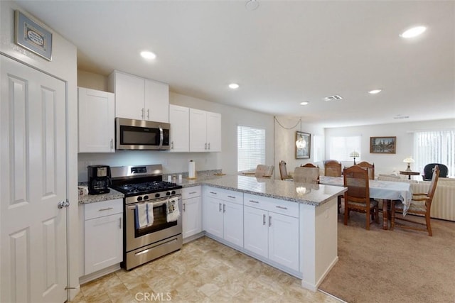 kitchen with a peninsula, white cabinets, light stone countertops, visible vents, and appliances with stainless steel finishes