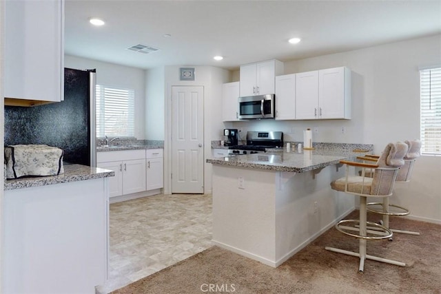kitchen with visible vents, a kitchen breakfast bar, a peninsula, white cabinetry, and stainless steel appliances