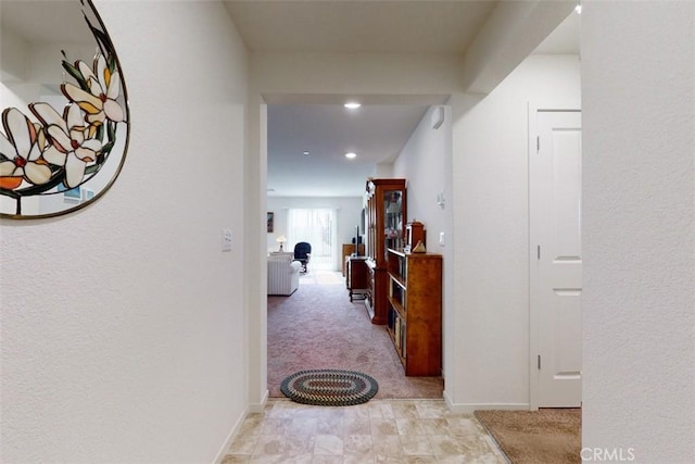 hallway with baseboards, recessed lighting, and light carpet