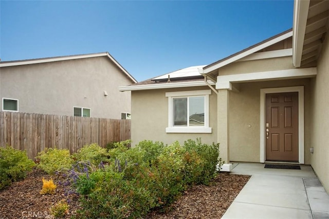 doorway to property featuring fence, roof mounted solar panels, and stucco siding