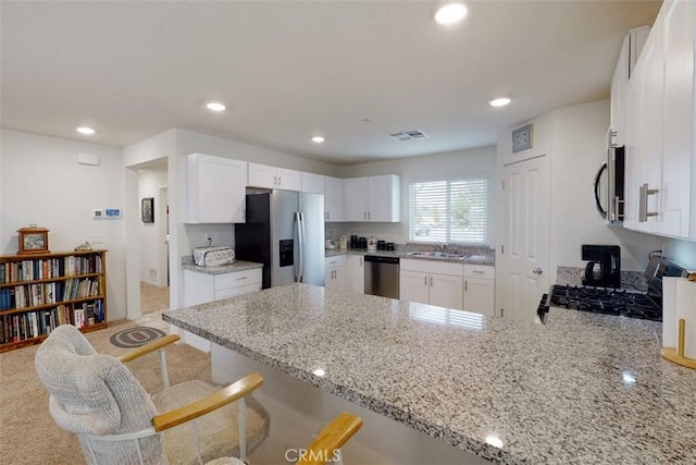 kitchen featuring recessed lighting, a peninsula, white cabinets, light stone countertops, and stainless steel appliances
