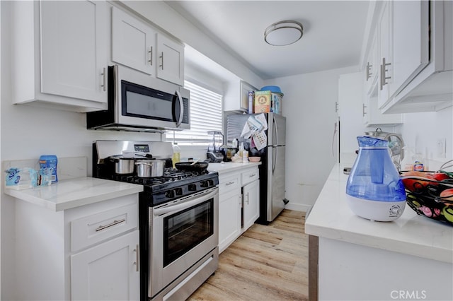 kitchen featuring appliances with stainless steel finishes, light wood-type flooring, white cabinets, and light stone counters