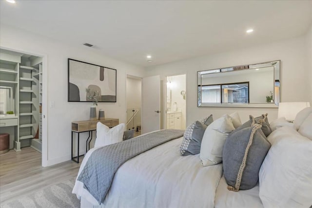 bedroom with a walk in closet, a closet, ensuite bath, and light wood-type flooring