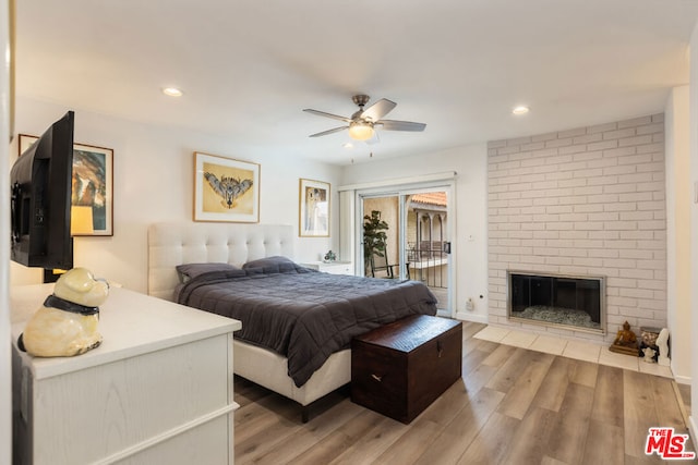 bedroom featuring a brick fireplace, access to outside, ceiling fan, and light hardwood / wood-style flooring