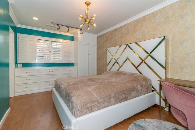 bedroom with hardwood / wood-style floors, crown molding, rail lighting, and a chandelier