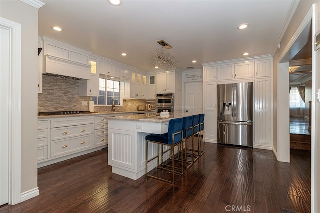 kitchen featuring dark wood-type flooring, a breakfast bar area, white cabinetry, stainless steel appliances, and a kitchen island with sink