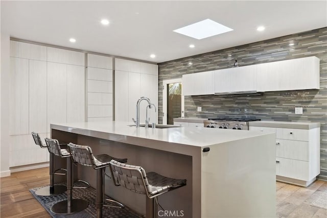 kitchen featuring a breakfast bar area, white cabinetry, light hardwood / wood-style flooring, a kitchen island with sink, and stove