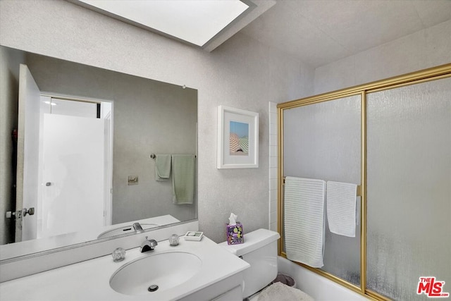 full bathroom featuring vanity, a skylight, toilet, and combined bath / shower with glass door