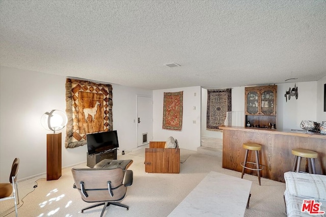 carpeted living room featuring a textured ceiling and bar area