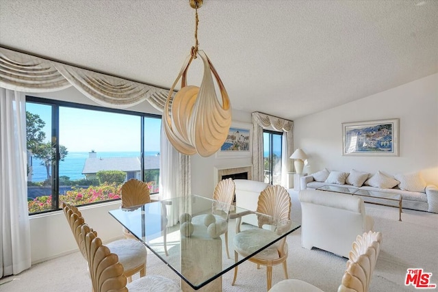 carpeted dining area with a water view, a tile fireplace, lofted ceiling, and plenty of natural light