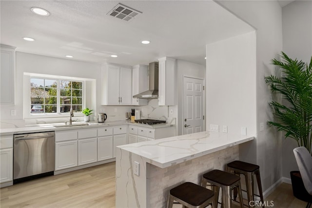 kitchen with stainless steel appliances, sink, wall chimney range hood, and white cabinets