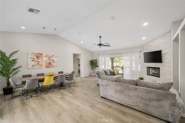 living room with vaulted ceiling, a stone fireplace, ceiling fan, and light hardwood / wood-style floors