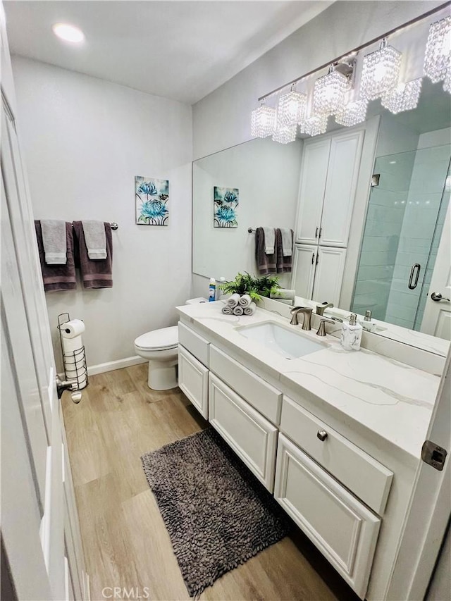 bathroom with wood-type flooring, toilet, a shower with door, and vanity