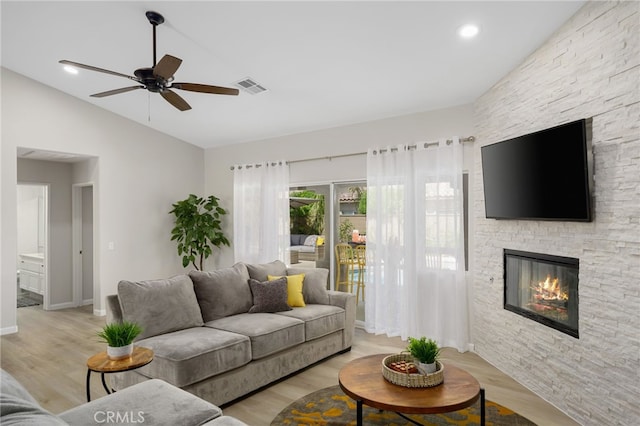 living room featuring lofted ceiling, a stone fireplace, ceiling fan, and light hardwood / wood-style flooring