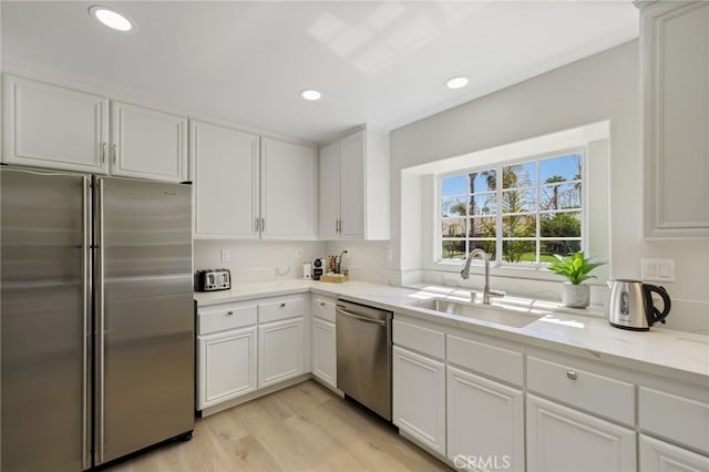 kitchen featuring sink, white cabinetry, stainless steel appliances, light hardwood / wood-style floors, and light stone countertops