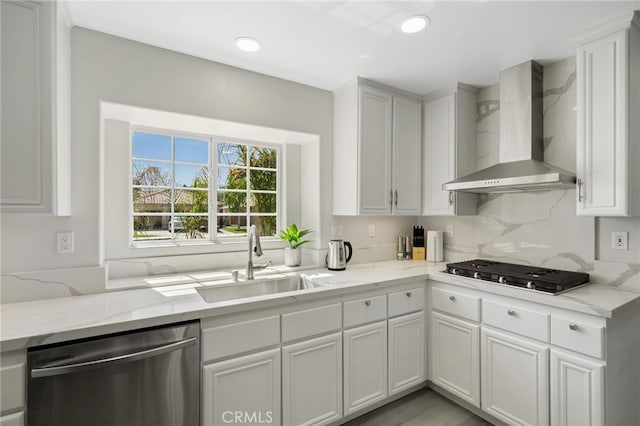 kitchen featuring white cabinetry, sink, stainless steel appliances, light stone countertops, and wall chimney range hood