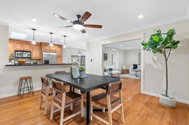 dining area featuring a skylight, ornamental molding, ceiling fan, and light hardwood / wood-style flooring