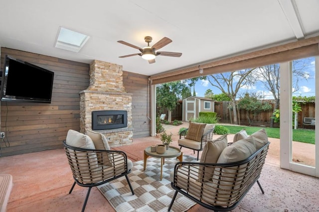 view of patio with ceiling fan, an outdoor living space with a fireplace, and a shed