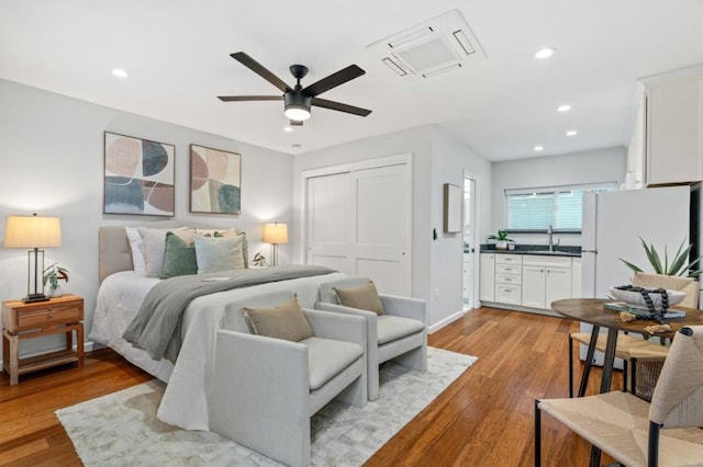 bedroom with sink, light hardwood / wood-style flooring, white fridge, ceiling fan, and a closet