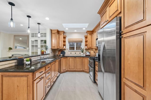 kitchen featuring sink, a skylight, appliances with stainless steel finishes, pendant lighting, and dark stone counters