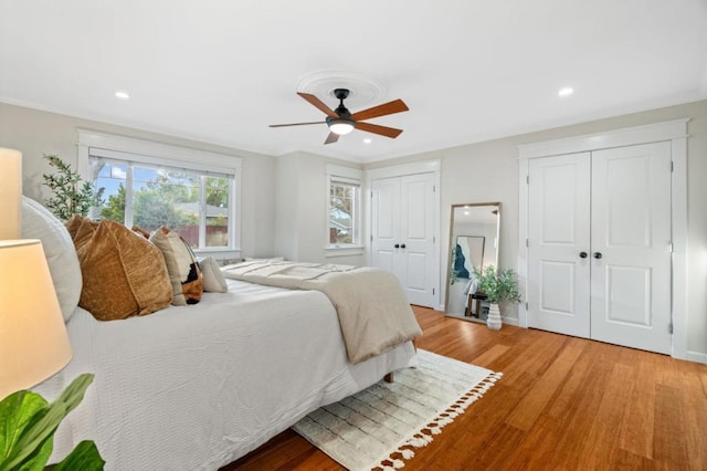 bedroom featuring multiple closets, crown molding, hardwood / wood-style flooring, and ceiling fan