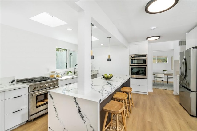 kitchen with white cabinetry, a center island, hanging light fixtures, light wood-type flooring, and appliances with stainless steel finishes