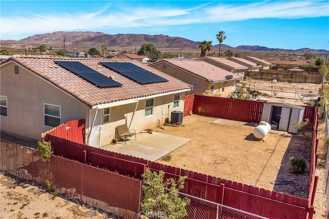 rear view of property with a storage shed, a mountain view, central AC, and solar panels