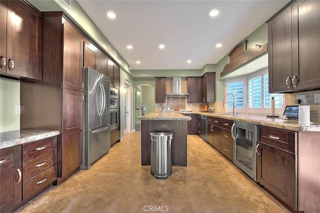 kitchen with a center island, stainless steel refrigerator, a kitchen breakfast bar, beverage cooler, and wall chimney range hood