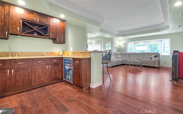 kitchen with sink, beverage cooler, dark hardwood / wood-style flooring, a kitchen bar, and a raised ceiling