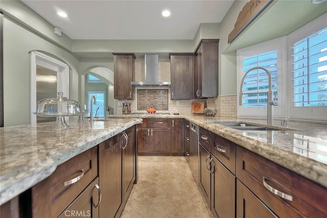 kitchen with light stone counters, sink, decorative backsplash, and wall chimney range hood