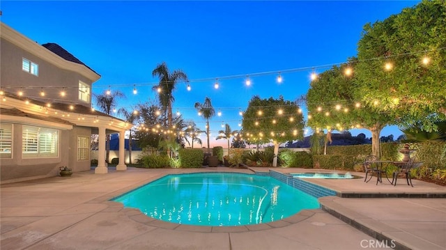 pool at dusk with an in ground hot tub and a patio area