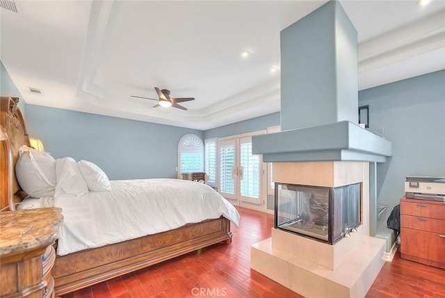 bedroom with ceiling fan, dark hardwood / wood-style floors, a fireplace, and a tray ceiling