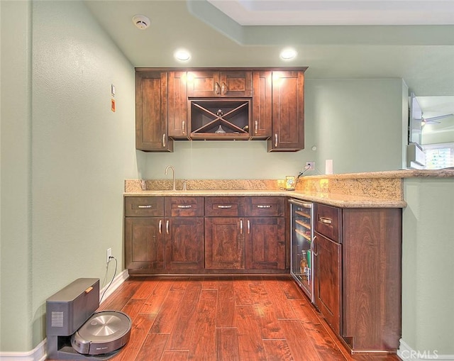 kitchen featuring dark hardwood / wood-style floors, sink, beverage cooler, light stone counters, and kitchen peninsula