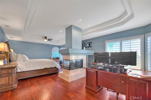 bedroom with ceiling fan, a fireplace, dark hardwood / wood-style floors, and a raised ceiling