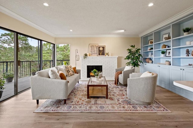 living room with built in features, a fireplace, ornamental molding, a textured ceiling, and light wood-type flooring