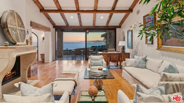 living room featuring lofted ceiling with beams, a premium fireplace, a water view, and light wood-type flooring