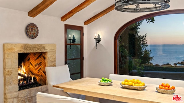 dining space with a water view, a fireplace, and beamed ceiling