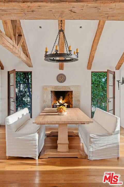 unfurnished dining area featuring an inviting chandelier, vaulted ceiling with beams, hardwood / wood-style floors, and a high end fireplace