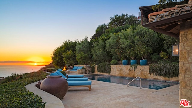 pool at dusk featuring a patio area, outdoor lounge area, and a water view