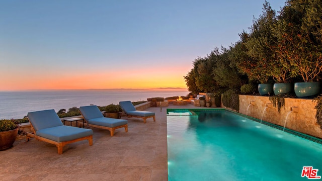 pool at dusk featuring a patio area and a water view