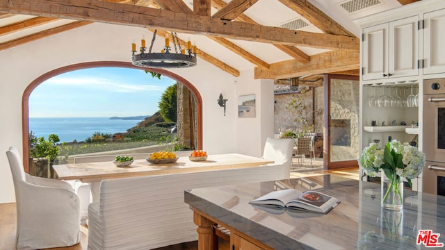 dining area featuring a notable chandelier, lofted ceiling with beams, and a water view