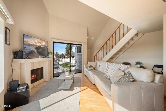 living room featuring high vaulted ceiling, a fireplace, and light hardwood / wood-style floors