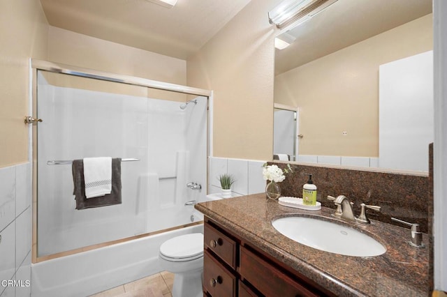 full bathroom featuring tile patterned floors, toilet, combined bath / shower with glass door, tile walls, and vanity